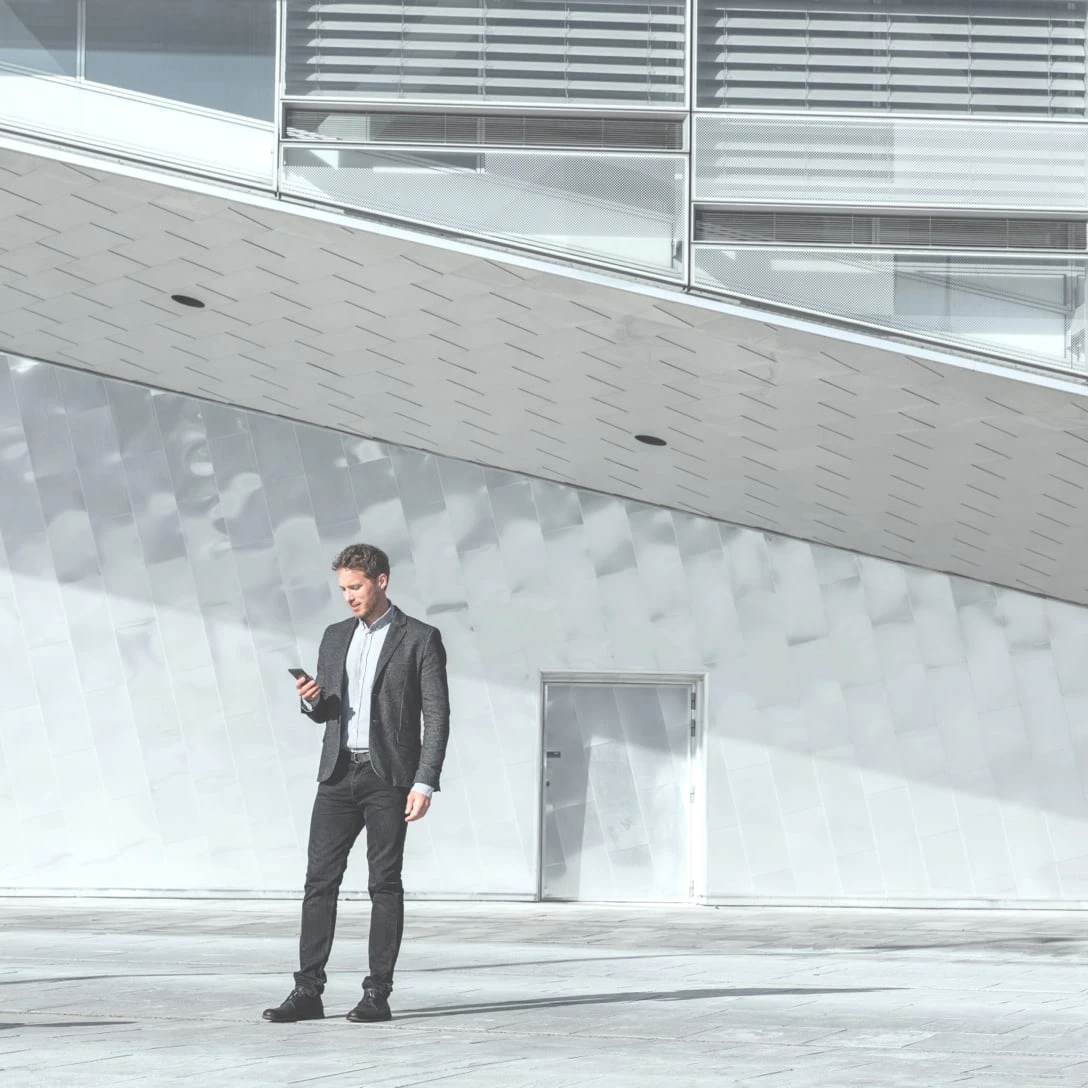 Person mit einem Smartphone in der Hand steht vor einem Gebäude